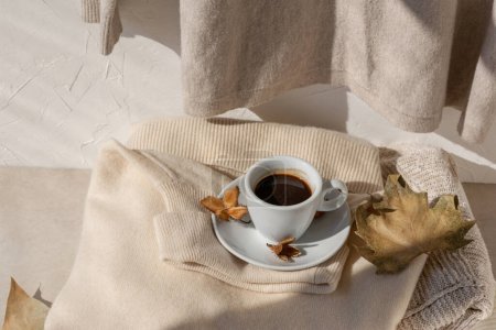 Photo for Autumn aesthetic still life with coffee cup, light brown fall leaves, light beige knitted sweaters in sunlight with natural shadow. Neutral pastel lifestyle autumn background. - Royalty Free Image