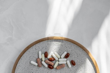 Photo for White and brown pills and capsules on gray plate and white table with abstract natural sun light shadows. Health care, medicine, pharmaceutical industry lifestyle minimal concept. - Royalty Free Image