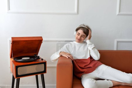 Photo for Teenager boy listening music wearing earphones near wooden turntable with vinyl record. - Royalty Free Image