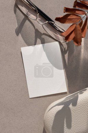 Photo for Aesthetic autumn business brand template, blank paper card, eyeglasses, fall leaves with shadows on neutral beige table background. - Royalty Free Image