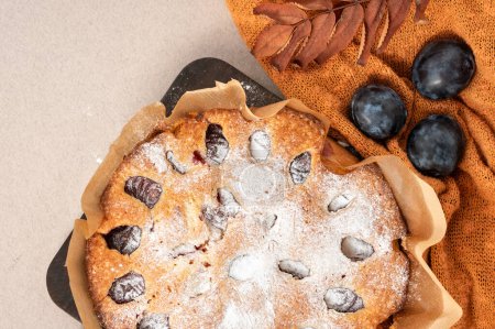 Photo for Autumn traditional bakery, Thanksgiving day treat. Pie, cake with plum, cinnamon and sugar powder on orange knitted cloth and beige table background. - Royalty Free Image