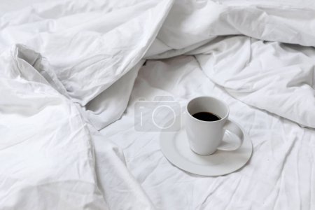 Photo for Cup with coffee drink standing on unmade bed with messy crumpled blanket, sheet and pillow. Lifestyle morning concept, coffee in bed. - Royalty Free Image