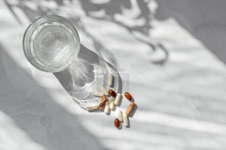 Photo for Wellness, healthcare, medicine, pharmaceutical industry concept. Assorted pills and capsules, glass with pure clean water on white marble table background with aesthetic sunlight shadows. - Royalty Free Image