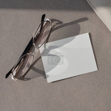 Photo for Blank paper card mockup and eyeglasses with sun light shadow on neutral background. Postcard, invitation, flyer or leaflet template. - Royalty Free Image