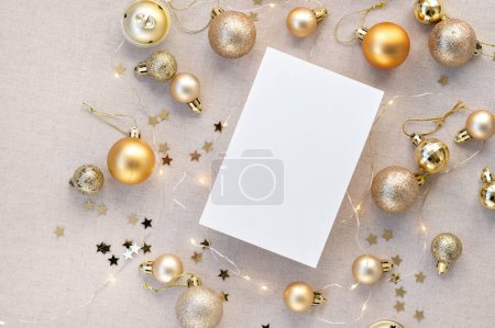 Photo for Aesthetic winter holiday business brand template. Blank paper card mockup and golden decoration balls, confetti and garland lights on beige background. New Year celebration postcard or invitation. - Royalty Free Image