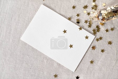 Photo for Blank paper card mockup on neutral beige linen tablecloth, gold star confetti scattered from bottle. Aesthetic holiday, New year postcard, invitation, business brand template. - Royalty Free Image