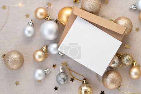 Photo for Blank paper card mockup and envelope, gold and silver ornaments, Christmas tree decoration balls, star confetti and garland lights on neutral beige linen background. Invitation, postcard template. - Royalty Free Image