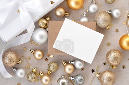 Photo for Christmas, New Year holiday congratulation postcard template. Blank paper card mockup, envelope, white present box, gold and silver ornaments, Christmas tree decoration balls on beige background. - Royalty Free Image