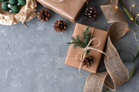 Photo for Christmas present boxes, wrapped in brown craft paper, decorated with pine cones and branches on gray textured table background. Sustainable rustic Christmas holiday backdrop, flat lay, copy space. - Royalty Free Image