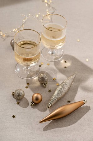 Téléchargez les photos : Concept de fête du Nouvel An esthétique, ornements en bronze et champagne, verres à vin avec vin mousseux, guirlandes floues sur fond de table beige neutre avec ombres. Concentration sélective. - en image libre de droit
