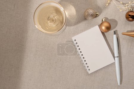 Foto de La planificación de objetivos para el Año Nuevo, pidiendo un deseo. Cuaderno abierto en blanco y pluma sobre fondo de mesa, copa de vino con vino espumoso, adornos navideños, sombras naturales. Colocación plana, espacio de copia. - Imagen libre de derechos