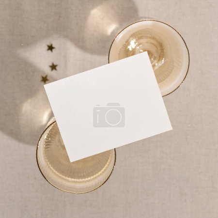 Photo for Blank paper business card mockup on wineglasses with sparkling wine, on neutral beige background with sunlight shadows. Invitation or postcard, holiday minimal branding template. - Royalty Free Image