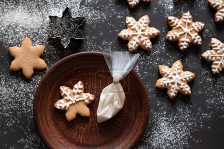 Photo for Making traditional Christmas ginger cookie. Star shape gingerbread cookie on black table background with flour and on plate, piping bag with sugar icing. Gingersnap cookie decoration, Selective focus. - Royalty Free Image