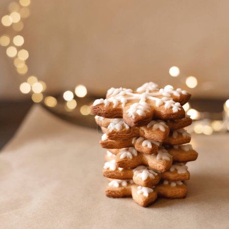 Photo for Sweet sugar gingerbread cookie with snowflake shape, decorated with sugar icing, blurred garland lights on background. Cozy winter home dessert, selective focus, lifestyle. - Royalty Free Image