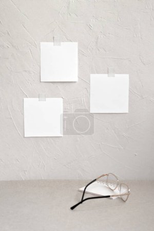Photo for Minimalist aesthetic home workspace, desktop with eyeglasses and notepad, textured plaster wall with empty paper sheets. Reminder, planner, schedule list for business brand or freelancer job. - Royalty Free Image