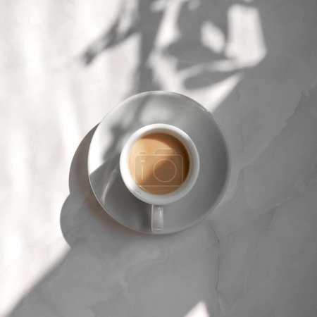 Téléchargez les photos : Concept minimaliste de bonne matinée esthétique, tasse à café en céramique blanche et soucoupe sur fond de table en marbre avec ombres de soleil géométriques et florales - en image libre de droit