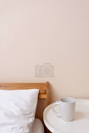Foto de Minimalista estilo de vida simple dormitorio diseño interior. Cama con almohada de lino blanco y manta, mesita de noche con taza de café, fondo de pared de melocotón ligero neutro vacío con espacio para copiar. - Imagen libre de derechos