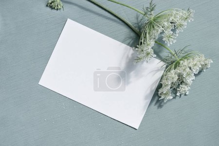 Photo for Beautiful white blooming flowers and blank paper card mockup on light blue textured cloth background. Aesthetic floral greeting postcard for Mothers day, Valentines day, wedding invitation template. - Royalty Free Image