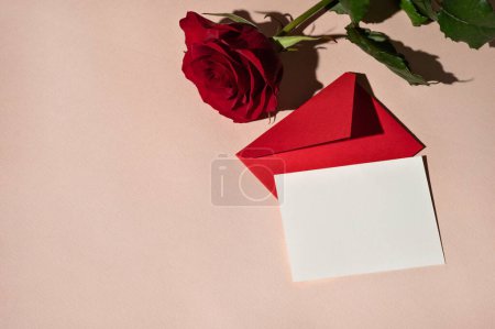 Photo for Blank paper card mockup, red envelope, rose flower on light peach background with harsh shadows. Luxury minimal holiday greeting card for birthday, Valentine day or wedding, date invitation template. - Royalty Free Image