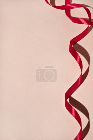 Foto de Cinta roja sobre fondo rosa pastel con sombras ásperas y luz brillante, telón de fondo festivo mínimo con espacio para copiar. - Imagen libre de derechos