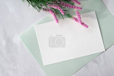 Photo for Spring aesthetic greeting postcard or invitation template, blank paper card, pink flowers, light mint green stationery on neutral marble table background, flat lay. - Royalty Free Image