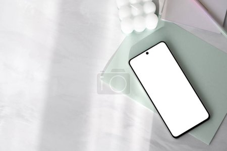 Smartphone with blank screen mockup, light pastel green paper stationery on white neutral marble table background with natural sunlight shadows , aesthetic template for social media.