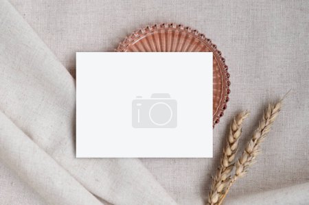 Foto de Maqueta de tarjeta en blanco sobre tela de lino, plato decorativo y tallos de trigo, plantilla estética para invitación o anuncio. - Imagen libre de derechos