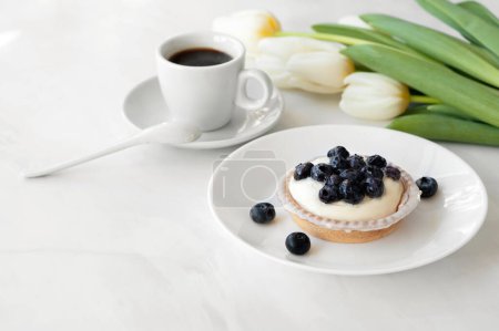 Téléchargez les photos : Délicieux et sucré petit déjeuner du matin, panna cotta cookie dessert aux bleuets, tasse à café et fleurs blanches sur la table. - en image libre de droit