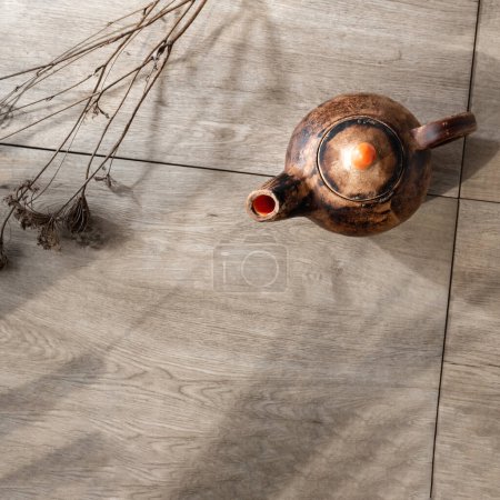 Foto de Elegante tetera de cerámica minimalista sobre un fondo de mesa de madera con hierba seca y sombras de luz solar, loza sostenible, concepto wabi sabi, espacio para copiar - Imagen libre de derechos