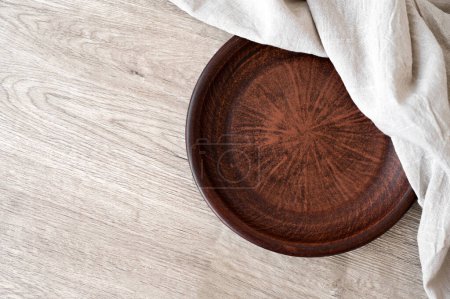 Foto de Auténtico plato de arcilla marrón hecho a mano, servilleta de lino beige neutro en la mesa de madera, vista superior, maqueta vacía para la colocación de productos alimenticios, espacio para copiar. - Imagen libre de derechos