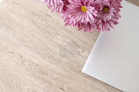 Foto de Fondo minimalista estético para la marca de negocios, portátil gris y flores de margarita rosa ramo en la mesa de madera beige neutro, vista superior, espacio de copia vacío. - Imagen libre de derechos