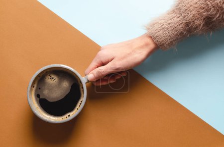 Téléchargez les photos : Main féminine tenant une tasse de café sur un fond bleu et brun. - en image libre de droit