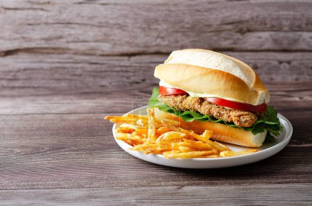 Téléchargez les photos : Sandwich milanesa avec tranches de tomate, laitue et mayonnaise, et frites dans une assiette blanche sur un fond en bois avec espace de copie. - en image libre de droit