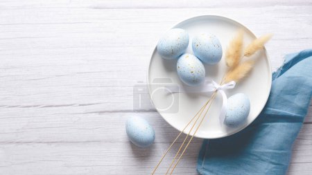 Téléchargez les photos : Ensemble de table de Pâques avec des œufs bleus et quelques épillets sur fond bois clair, une serviette bleue et un espace de copie. - en image libre de droit