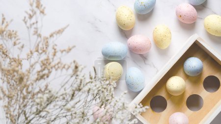 Téléchargez les photos : Œufs de Pâques colorés avec des taches dorées dans une boîte en bois sur un fond de marbre blanc et quelques fleurs. - en image libre de droit