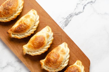 Typical Argentinian beef empanadas on a wooden board on white marble background. 