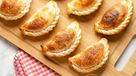 Argentinian beef empanadas on a wooden board on marble background and a red and white napkin. 