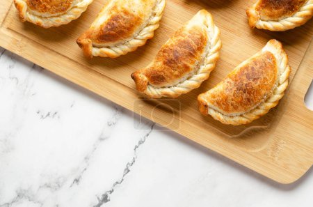 Argentinian beef empanadas on a wooden board on marble background. 