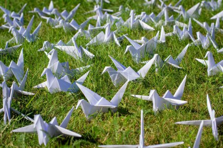 Foto de Japonés plegado grúas de origami sobre hierba fresca. Cientos de pájaros de papel hechos a mano en el campo verde con espacio de copia. 1000 mil tema de escultura de grúa tsuru. Símbolo de paz, fe, salud, deseos y esperanza - Imagen libre de derechos
