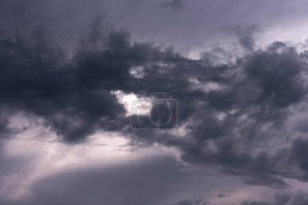 Photo for The sky is covered with a thin layer of dark gray clouds. Sunlight is visible through the clouds. - Royalty Free Image