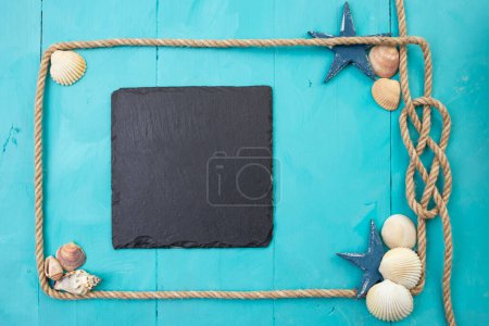 Téléchargez les photos : Jute rope frame with a knot, sea shells, stars and a square black stone slab on blue acrylic wooden boards. - en image libre de droit