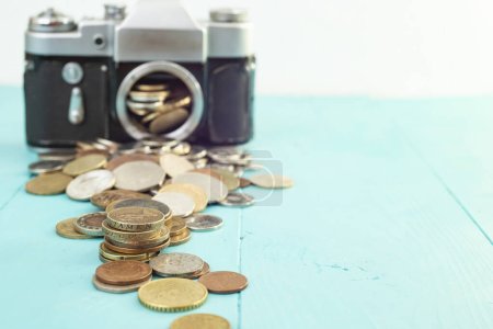 Defocused vintage camera with coins on the foreground, on blue background, soft focus close up