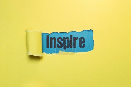inspire word written with stamp letters, on blue paper seen thru ripped yellow paper strip