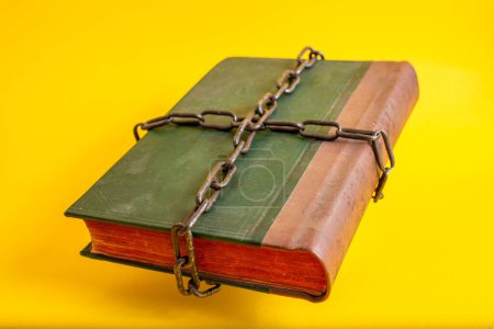 Téléchargez les photos : Vieille bible verte avec des pages rouges liées par des chaînes épaisses, flottant sur fond jaune - en image libre de droit