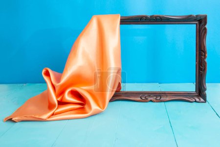 Téléchargez les photos : Cadre en bois vide dévoilé par un rideau en satin orange, sur fond bleu - en image libre de droit