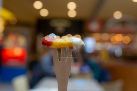 Foto de Wooden fork with a potato chip, dipped in mayonnaise and ketchup, with a restaurant and bokeh balls in the background, soft  focus close up - Imagen libre de derechos