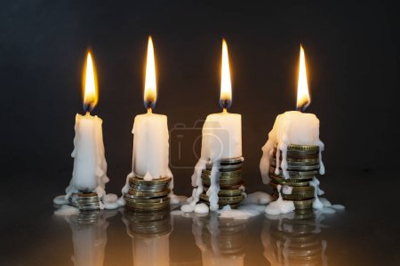 Téléchargez les photos : White candles  burning on top on coin stacks, on dark background. More money, less life metaphor - en image libre de droit