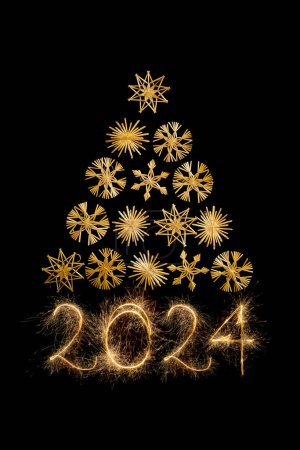 Foto de Triángulo del árbol de Navidad hecho con copos de nieve de paja y 2024 año nuevo escrito con bengalas aisladas sobre fondo negro - Imagen libre de derechos