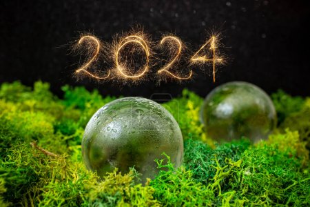 Téléchargez les photos : 2024 nombre écrit avec des étincelles dorées à côté de sphères de verre sur lichen vert avec fond noir, mise au point douce gros plan - en image libre de droit