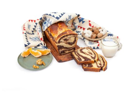Photo for Cozonac, Romanian traditional sweet bread with walnut filling, sliced , with a glass of milk and patterned cloth, side view - Royalty Free Image